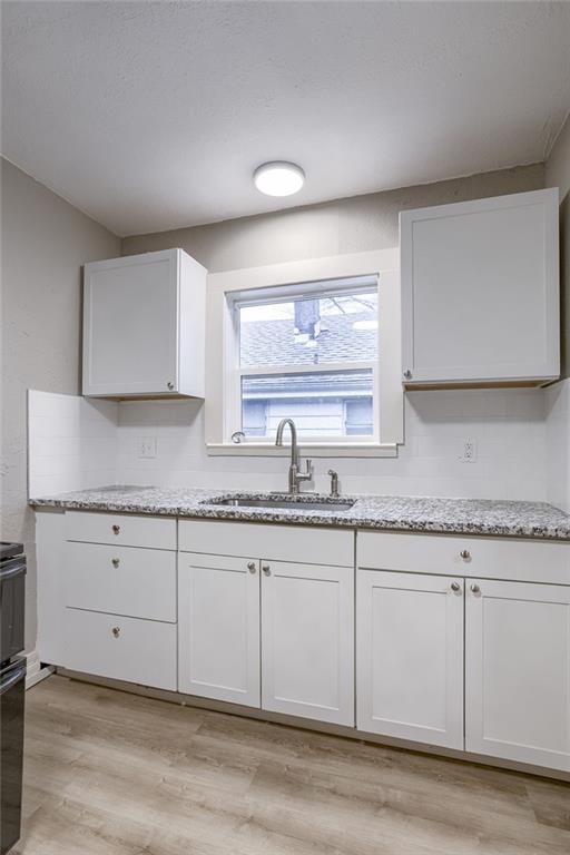 kitchen featuring white cabinetry, light stone countertops, and sink