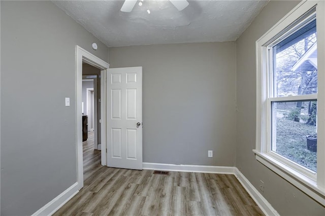 empty room with ceiling fan, a textured ceiling, and light wood-type flooring