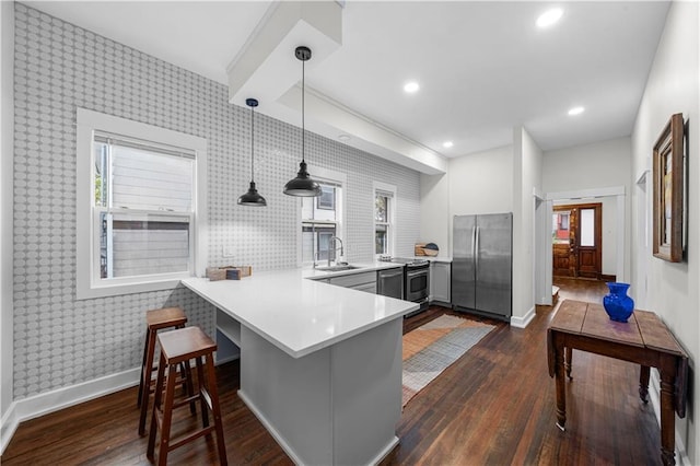 kitchen with stainless steel fridge, kitchen peninsula, sink, and hanging light fixtures