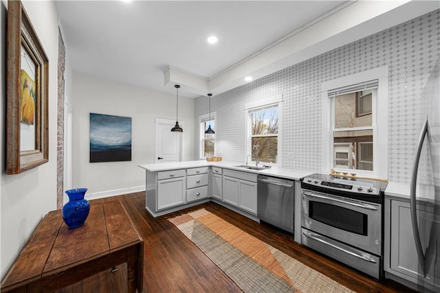 kitchen featuring dark wood-type flooring, sink, appliances with stainless steel finishes, kitchen peninsula, and pendant lighting