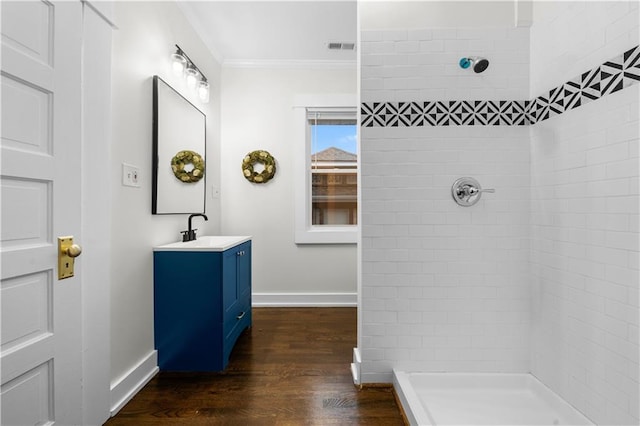 bathroom featuring a tile shower, hardwood / wood-style floors, crown molding, and vanity