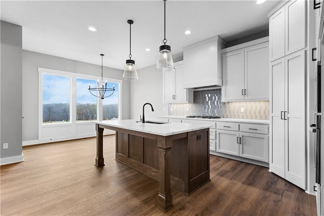 kitchen featuring a breakfast bar area, white cabinets, custom exhaust hood, hanging light fixtures, and a center island with sink