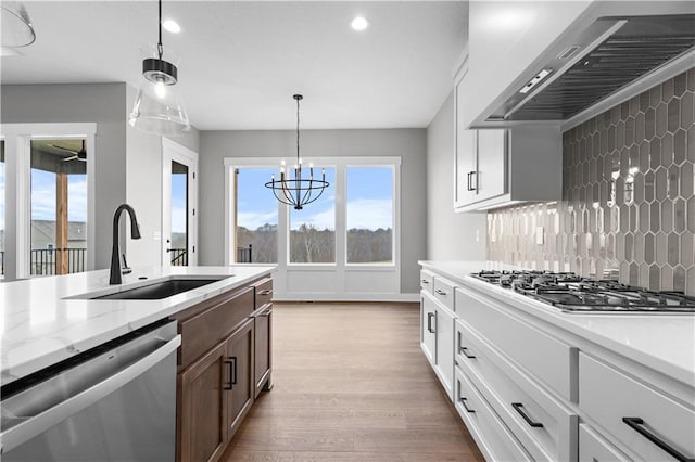 kitchen with sink, white cabinetry, hanging light fixtures, stainless steel appliances, and wall chimney range hood