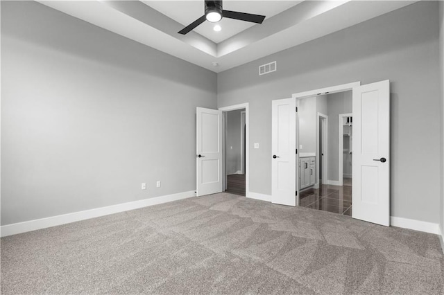 unfurnished bedroom featuring a raised ceiling, dark colored carpet, and ceiling fan