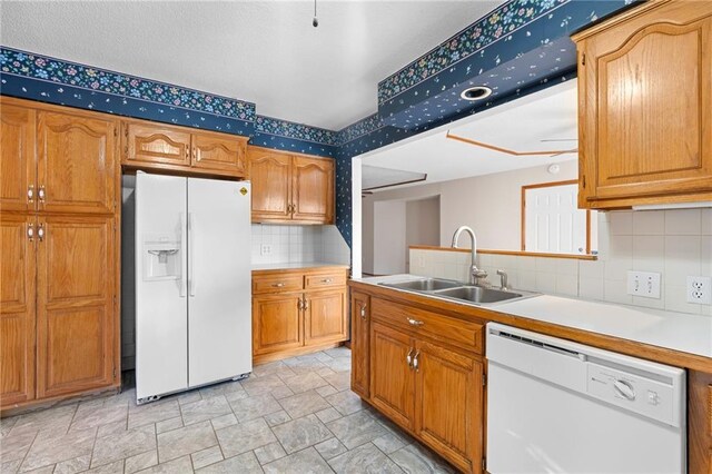 kitchen featuring white appliances, brown cabinetry, light countertops, and a sink