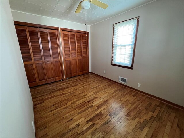 unfurnished bedroom with visible vents, ceiling fan, baseboards, multiple closets, and wood finished floors