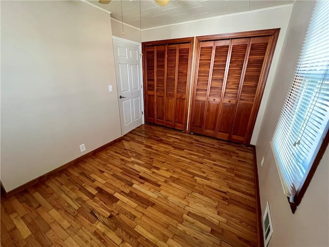 unfurnished bedroom with visible vents, multiple closets, wood finished floors, baseboards, and ceiling fan