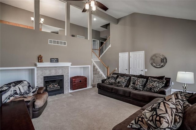 carpeted living room featuring a tiled fireplace, visible vents, stairs, and a ceiling fan