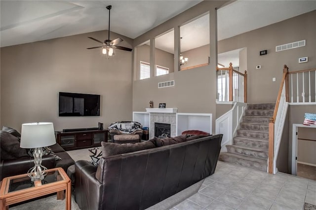 living area featuring stairs, visible vents, a fireplace, and ceiling fan with notable chandelier