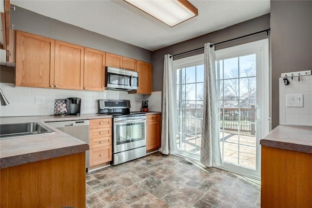 kitchen with visible vents, backsplash, appliances with stainless steel finishes, stone finish floor, and a sink