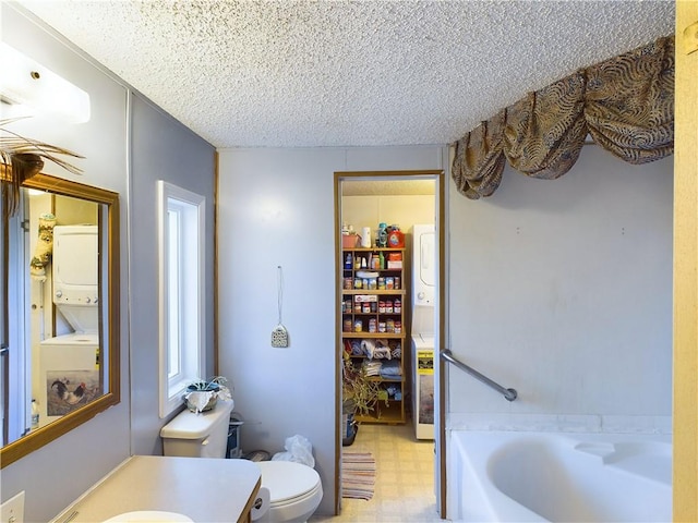 bathroom featuring stacked washer and dryer, vanity, a textured ceiling, a tub, and toilet