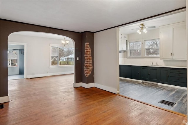 unfurnished dining area with crown molding, sink, ceiling fan with notable chandelier, and light wood-type flooring