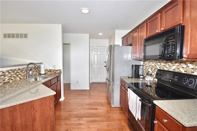 kitchen with sink, backsplash, black appliances, light stone countertops, and light wood-type flooring