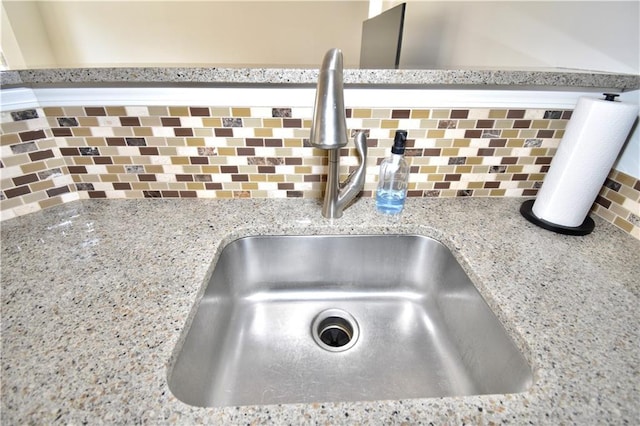 interior details featuring light stone countertops, sink, and backsplash