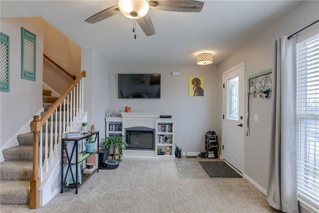 entryway featuring baseboards, a glass covered fireplace, ceiling fan, carpet, and stairs