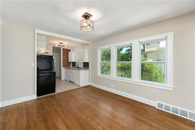 kitchen with sink, range, black refrigerator, light hardwood / wood-style floors, and white cabinets