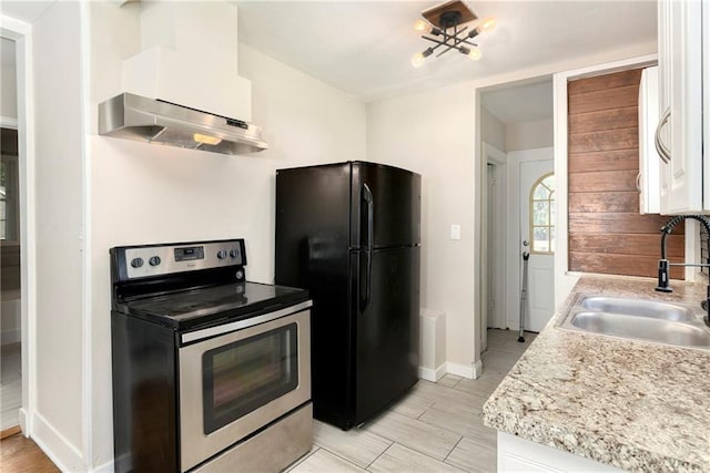 kitchen featuring wall chimney exhaust hood, sink, black fridge, stainless steel range with electric stovetop, and white cabinets