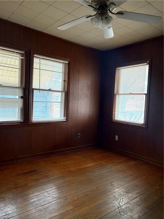 empty room with wood-type flooring, wooden walls, and ceiling fan