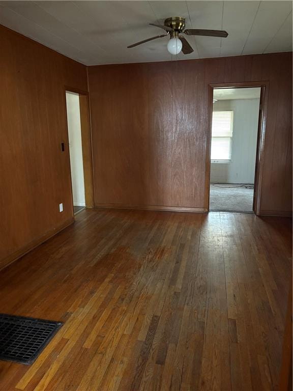 empty room with hardwood / wood-style flooring, ceiling fan, and wood walls