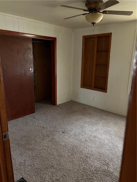 carpeted empty room featuring wooden walls and ceiling fan