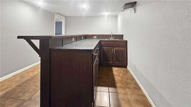 bar with sink, light tile patterned floors, and dark brown cabinetry