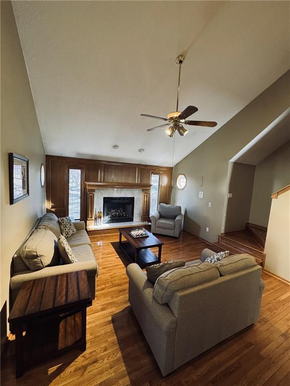 living room with vaulted ceiling, a fireplace, wood finished floors, and a ceiling fan