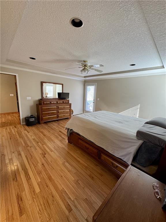 bedroom featuring light wood-style floors, ornamental molding, a ceiling fan, and a textured ceiling