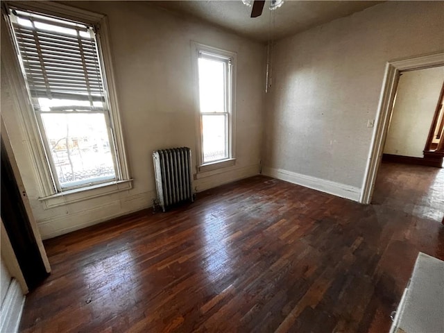 empty room with plenty of natural light, dark wood-type flooring, and radiator