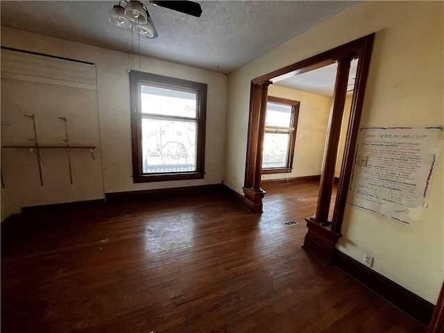 interior space with ceiling fan, ornate columns, dark hardwood / wood-style floors, and a textured ceiling