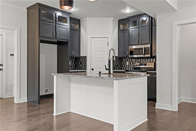 kitchen with light stone countertops, appliances with stainless steel finishes, a kitchen island with sink, and dark hardwood / wood-style flooring