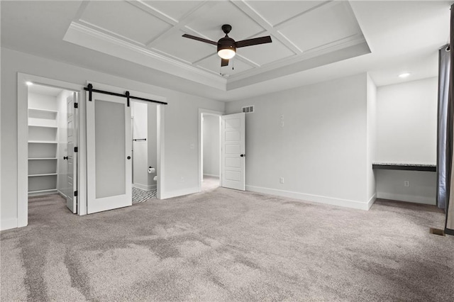 unfurnished bedroom with ceiling fan, carpet, coffered ceiling, a walk in closet, and a barn door