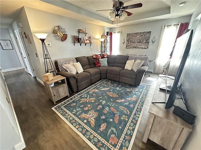 living room featuring a tray ceiling, dark wood-type flooring, and ceiling fan