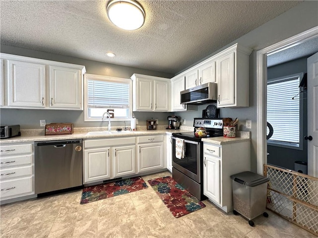 kitchen with sink, a textured ceiling, stainless steel appliances, and white cabinets