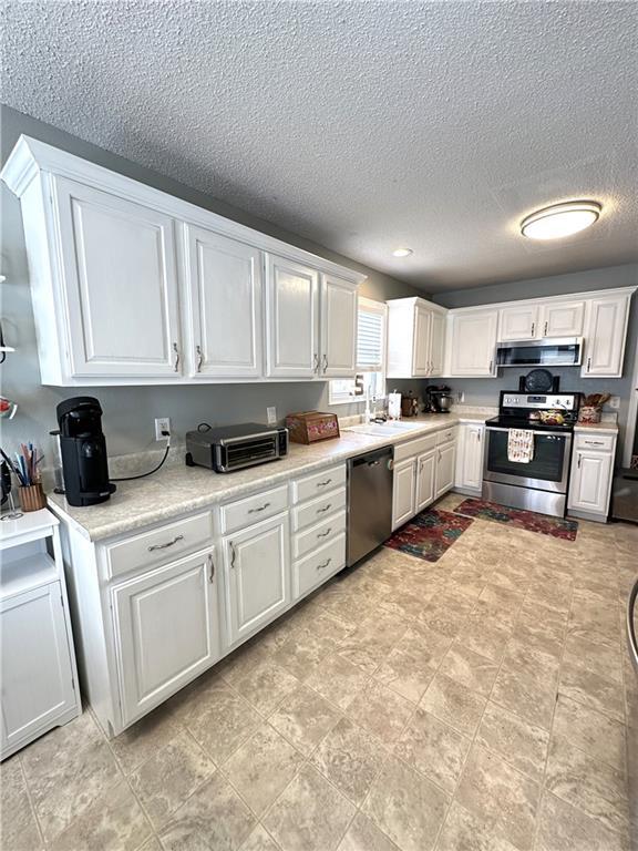 kitchen with extractor fan, sink, white cabinets, stainless steel appliances, and a textured ceiling