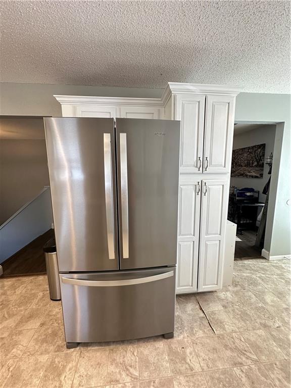 room details featuring a textured ceiling, stainless steel fridge, and white cabinets