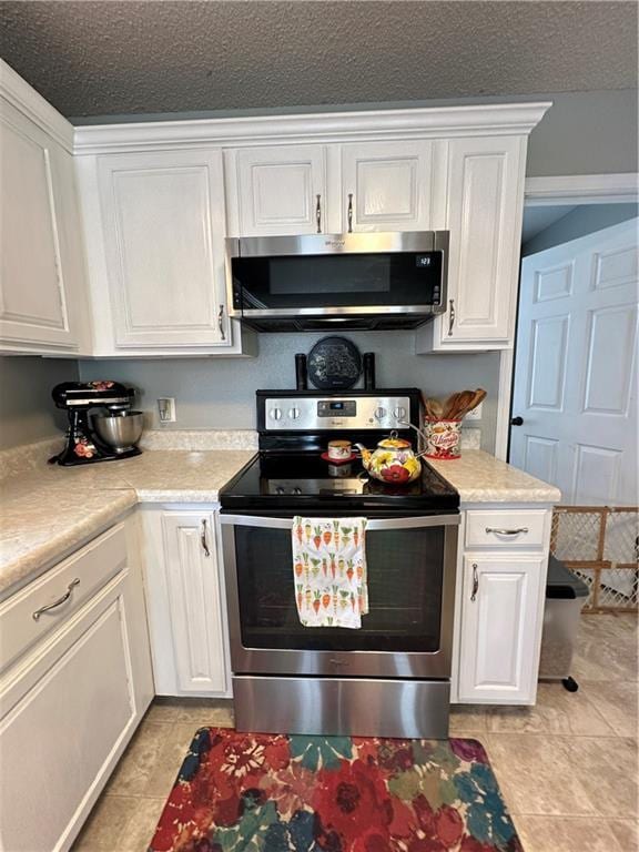 kitchen with light tile patterned floors, a textured ceiling, stainless steel appliances, and white cabinets