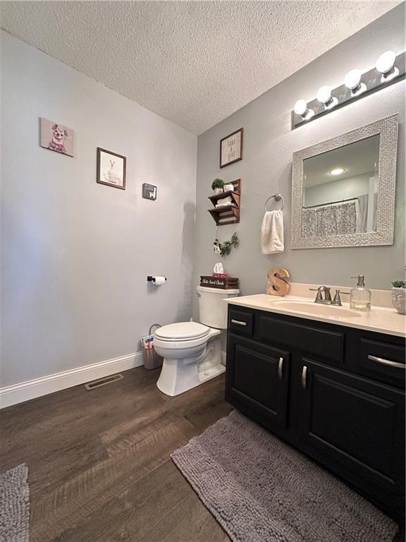 bathroom featuring hardwood / wood-style flooring, vanity, toilet, and a textured ceiling