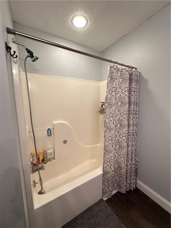 bathroom with hardwood / wood-style flooring, shower / tub combo with curtain, and a textured ceiling