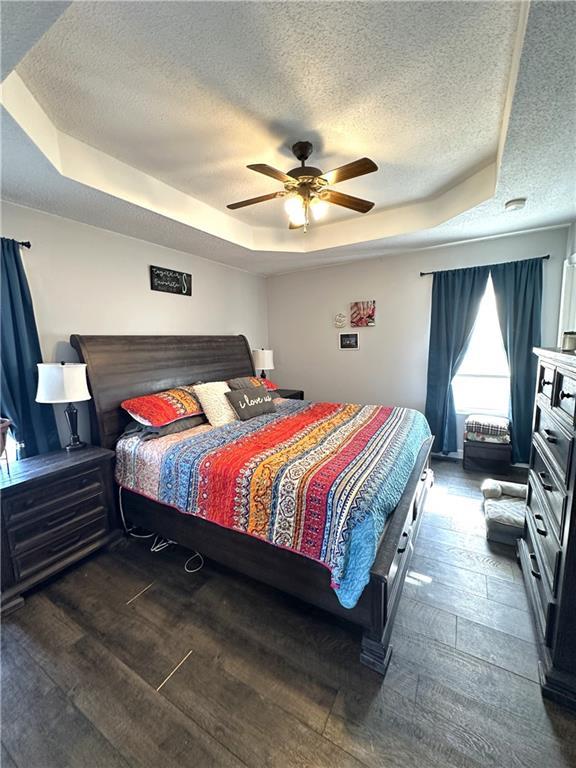 bedroom featuring dark wood-type flooring, ceiling fan, a tray ceiling, a fireplace, and a textured ceiling