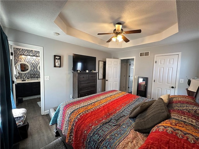 bedroom with ceiling fan, dark hardwood / wood-style floors, a textured ceiling, and a tray ceiling