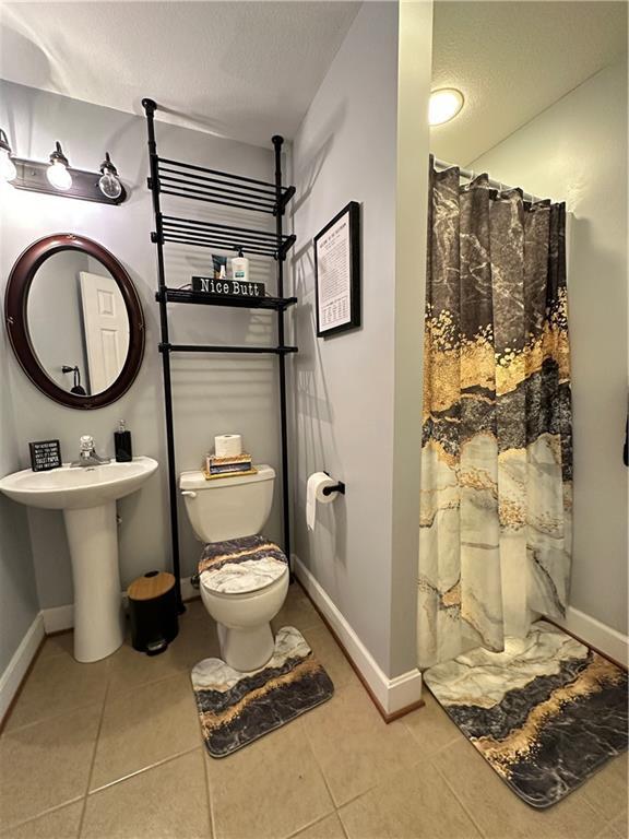 bathroom featuring toilet, sink, a shower with curtain, a textured ceiling, and tile patterned flooring