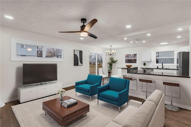 living room with sink, ceiling fan with notable chandelier, light hardwood / wood-style floors, and a textured ceiling