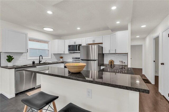 kitchen with appliances with stainless steel finishes, sink, a breakfast bar area, dark stone countertops, and white cabinets