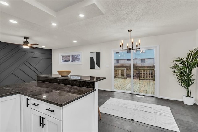 kitchen featuring ceiling fan with notable chandelier, dark stone countertops, a textured ceiling, white cabinets, and decorative light fixtures