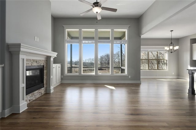 unfurnished living room with ceiling fan with notable chandelier and dark wood-type flooring