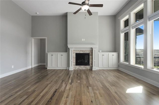 unfurnished living room with ceiling fan, a stone fireplace, and hardwood / wood-style floors