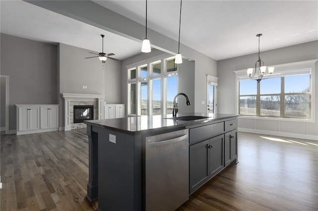 kitchen featuring a stone fireplace, sink, decorative light fixtures, stainless steel dishwasher, and an island with sink