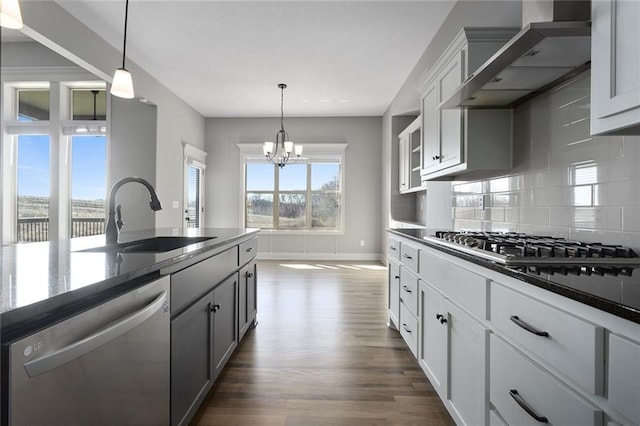 kitchen featuring wall chimney range hood, sink, appliances with stainless steel finishes, tasteful backsplash, and decorative light fixtures