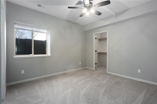 unfurnished bedroom with light carpet, a spacious closet, a closet, and ceiling fan