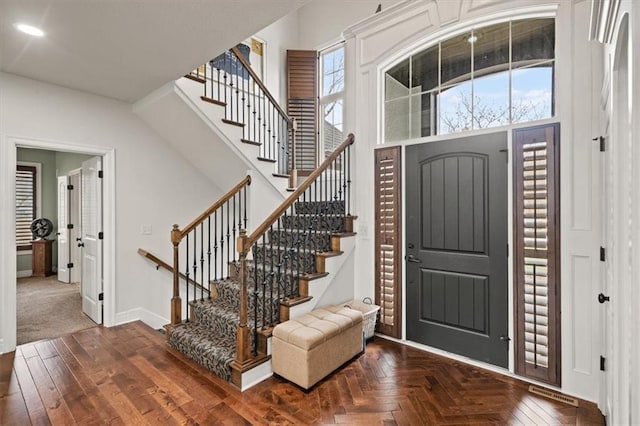 foyer with a high ceiling, a wealth of natural light, and dark parquet floors